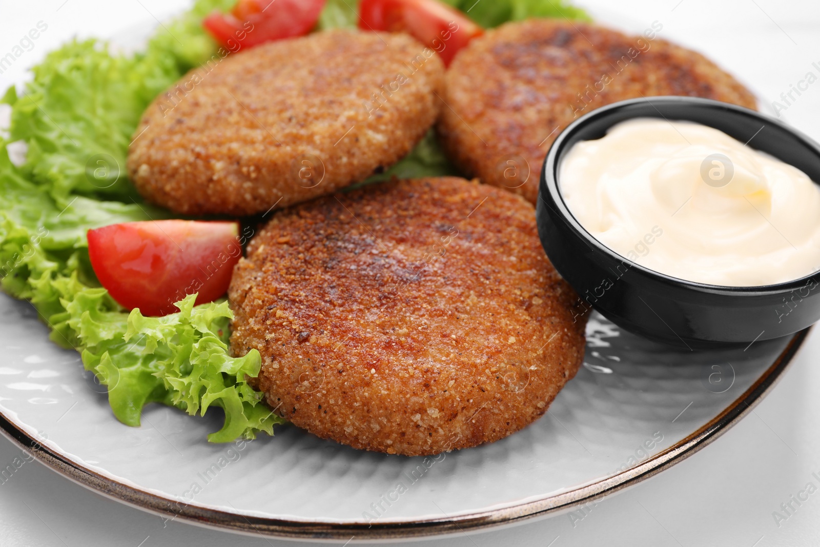 Photo of Delicious vegan cutlets, lettuce, tomato and sauce on white table, closeup