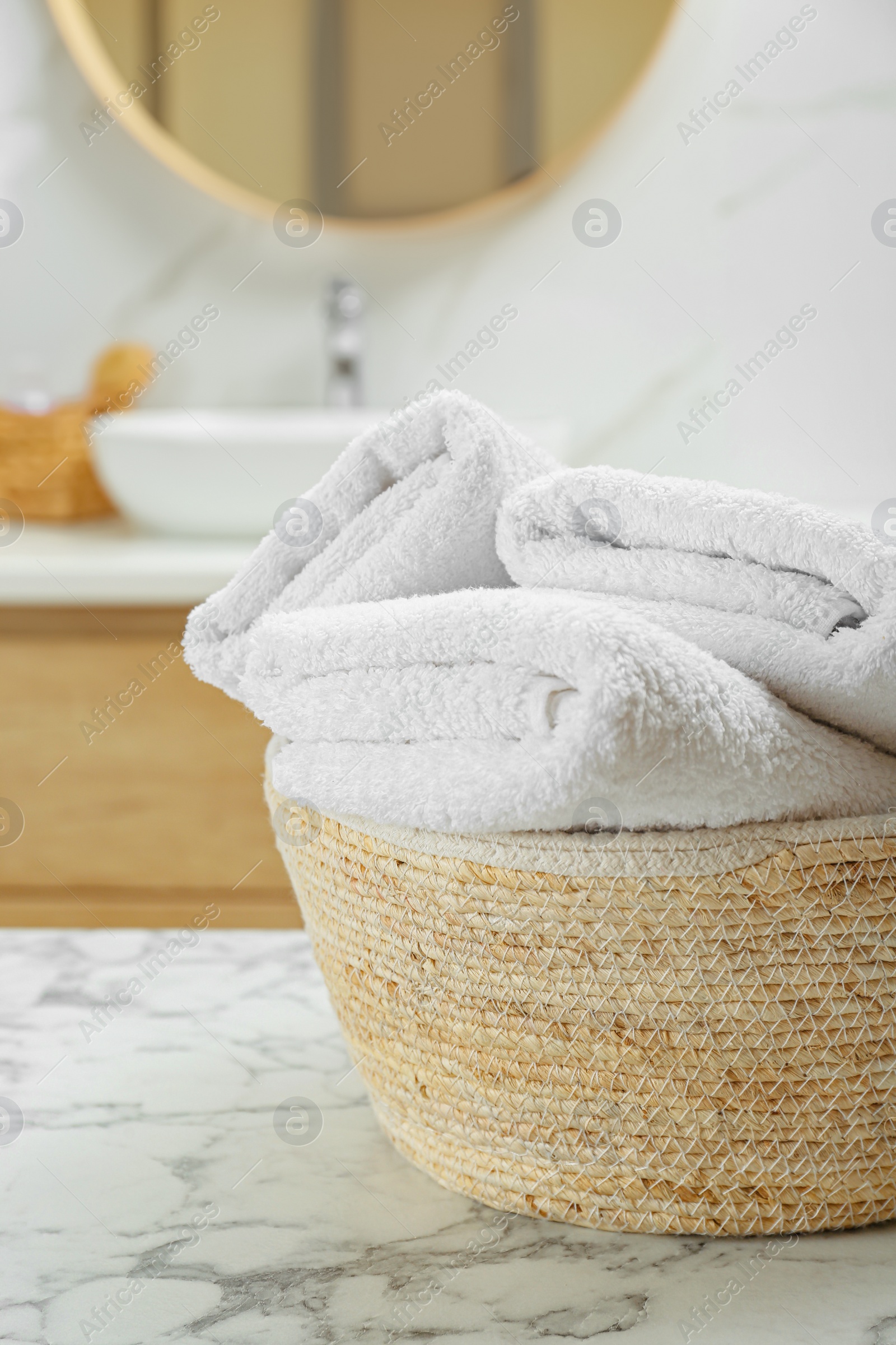 Photo of Wicker basket with folded bath towels on white marble table in bathroom