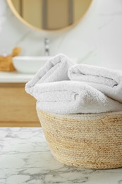 Photo of Wicker basket with folded bath towels on white marble table in bathroom