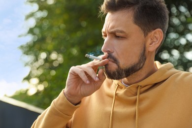 Handsome mature man smoking cigarette outdoors on sunny day