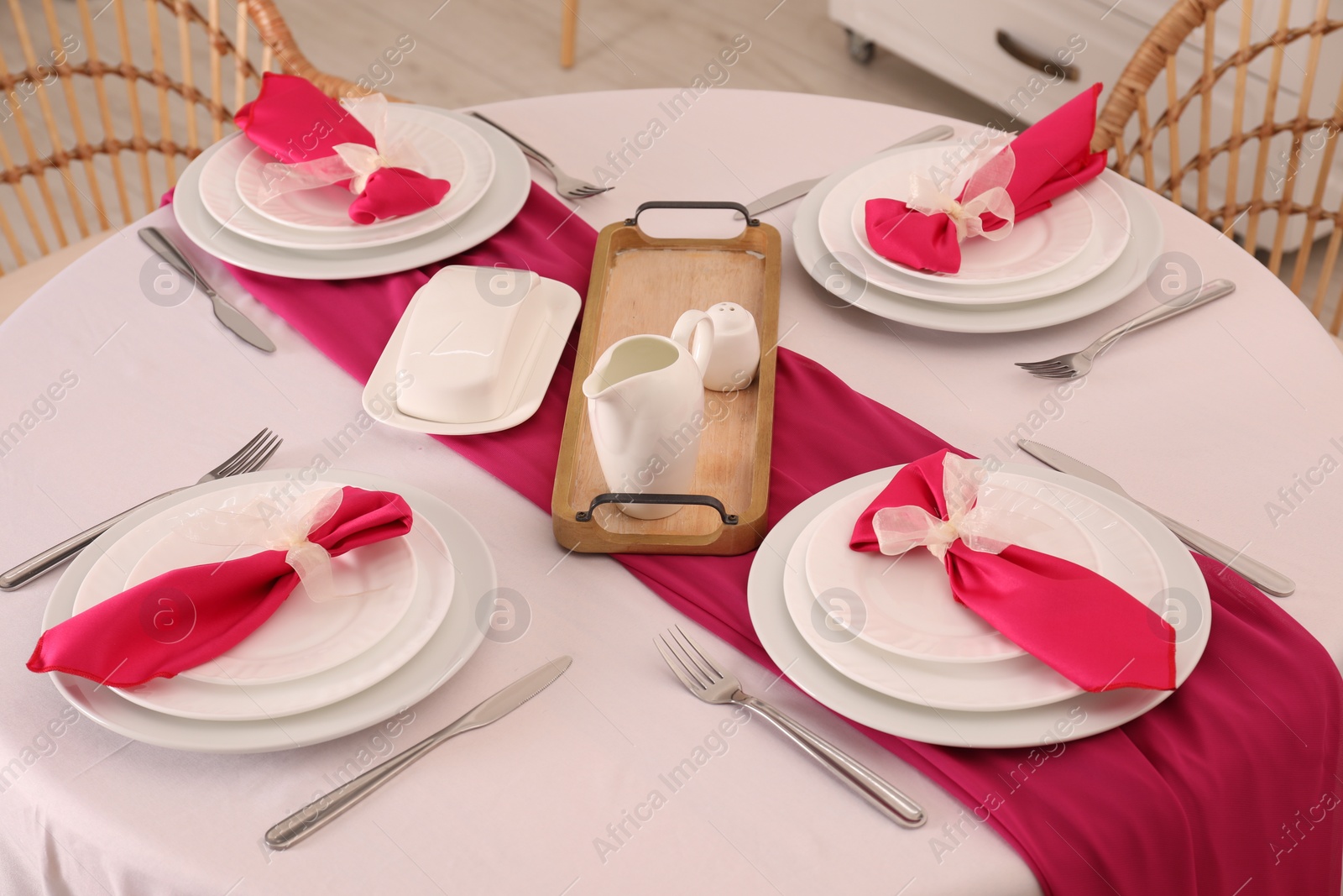 Photo of Color accent table setting. Plates, cutlery and pink napkins in dining room