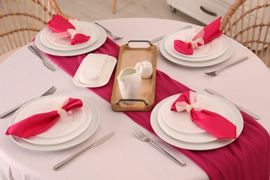 Photo of Color accent table setting. Plates, cutlery and pink napkins in dining room