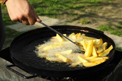 Photo of Man cooking delicious potato wedges on frying pan outdoors, closeup