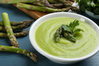 Photo of Delicious asparagus soup served on blue wooden table, closeup