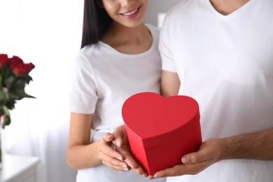 Photo of Lovely couple with gift box at home, closeup. Valentine's day celebration