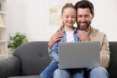 Photo of Happy man and his daughter with laptop on sofa at home. Space for text