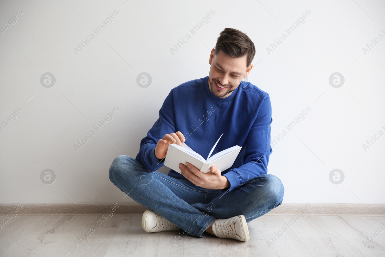 Photo of Handsome man reading book on floor near wall