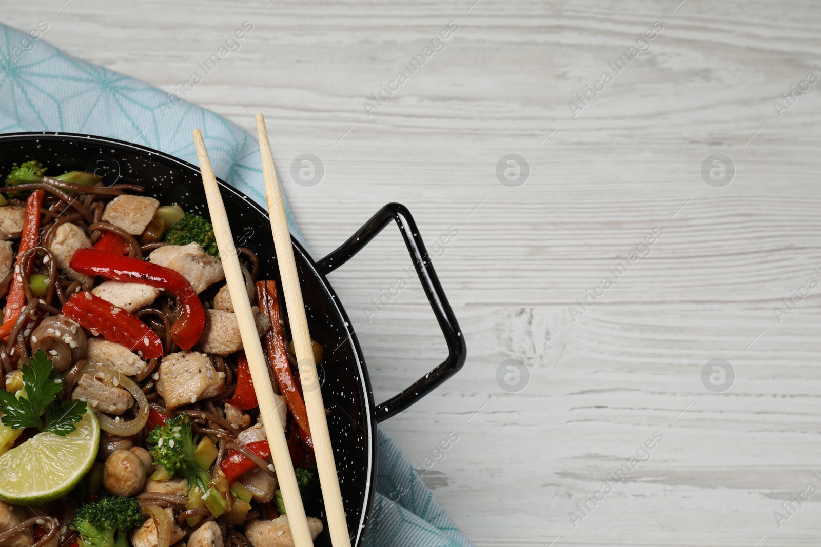 Photo of Stir-fry. Tasty noodles with meat in wok and chopsticks on white wooden table, top view. Space for text