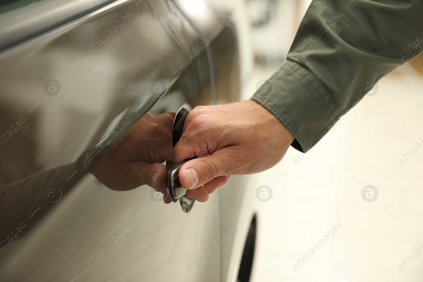 Photo of Young man opening car door in modern auto dealership, closeup