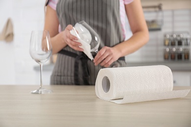 Woman wiping wine glass with paper towel in kitchen, closeup