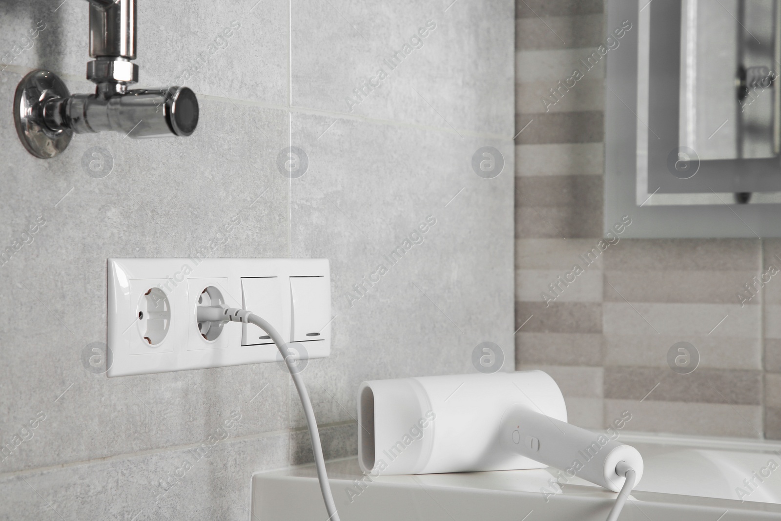 Photo of Hairdryer plugged into power socket on light grey wall in bathroom, space for text