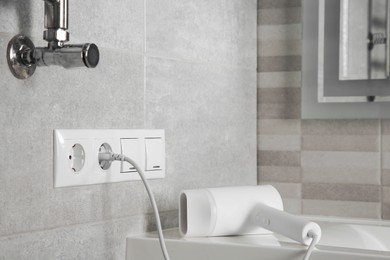 Photo of Hairdryer plugged into power socket on light grey wall in bathroom, space for text