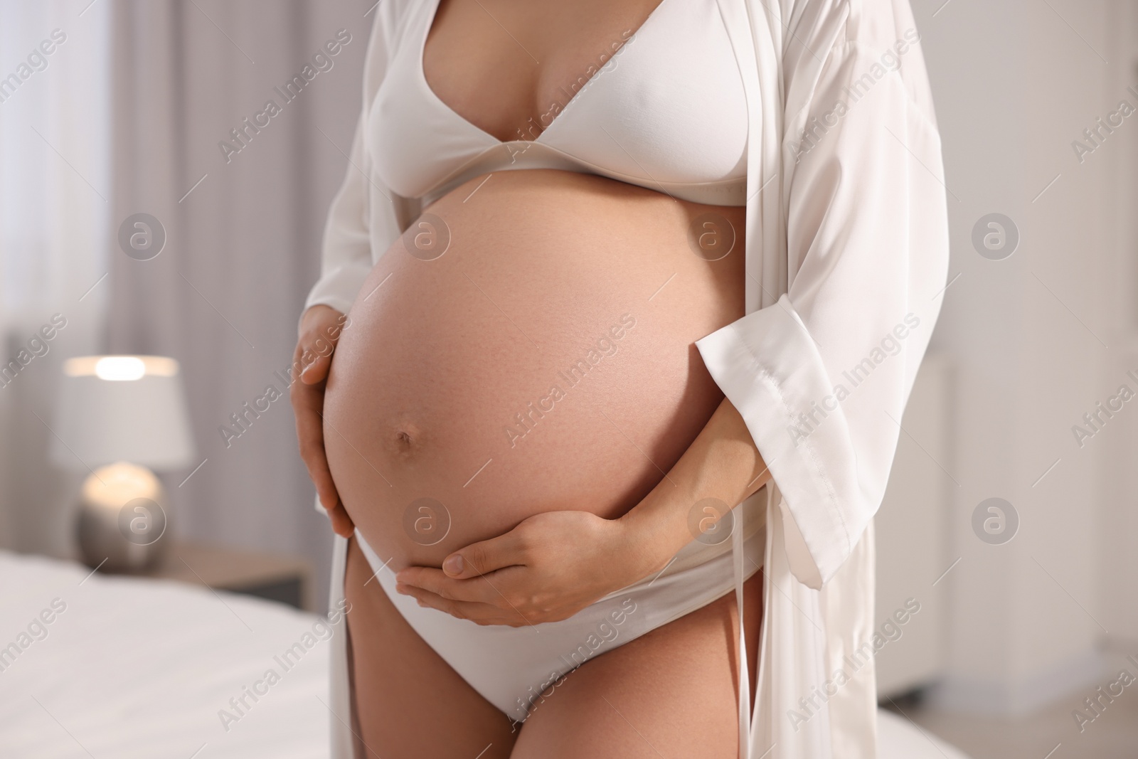 Photo of Pregnant woman wearing stylish comfortable underwear and robe in bedroom, closeup