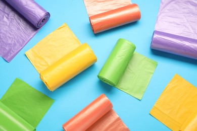 Rolls of different garbage bags on light blue background, flat lay