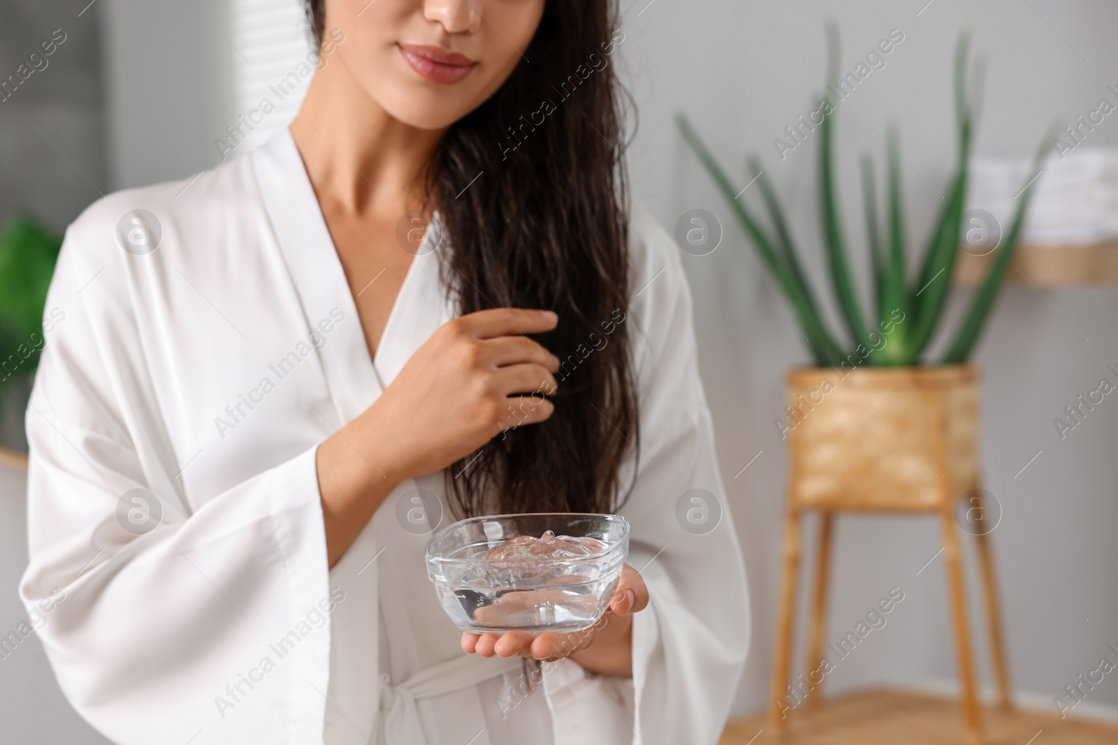 Photo of Young woman holding bowl of aloe hair mask indoors, closeup. Space for text