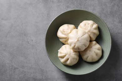 Delicious bao buns (baozi) in bowl on grey textured table, top view. Space for text