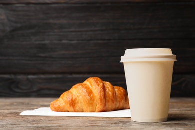 Paper cup with coffee and croissant on wooden table. Mockup for design