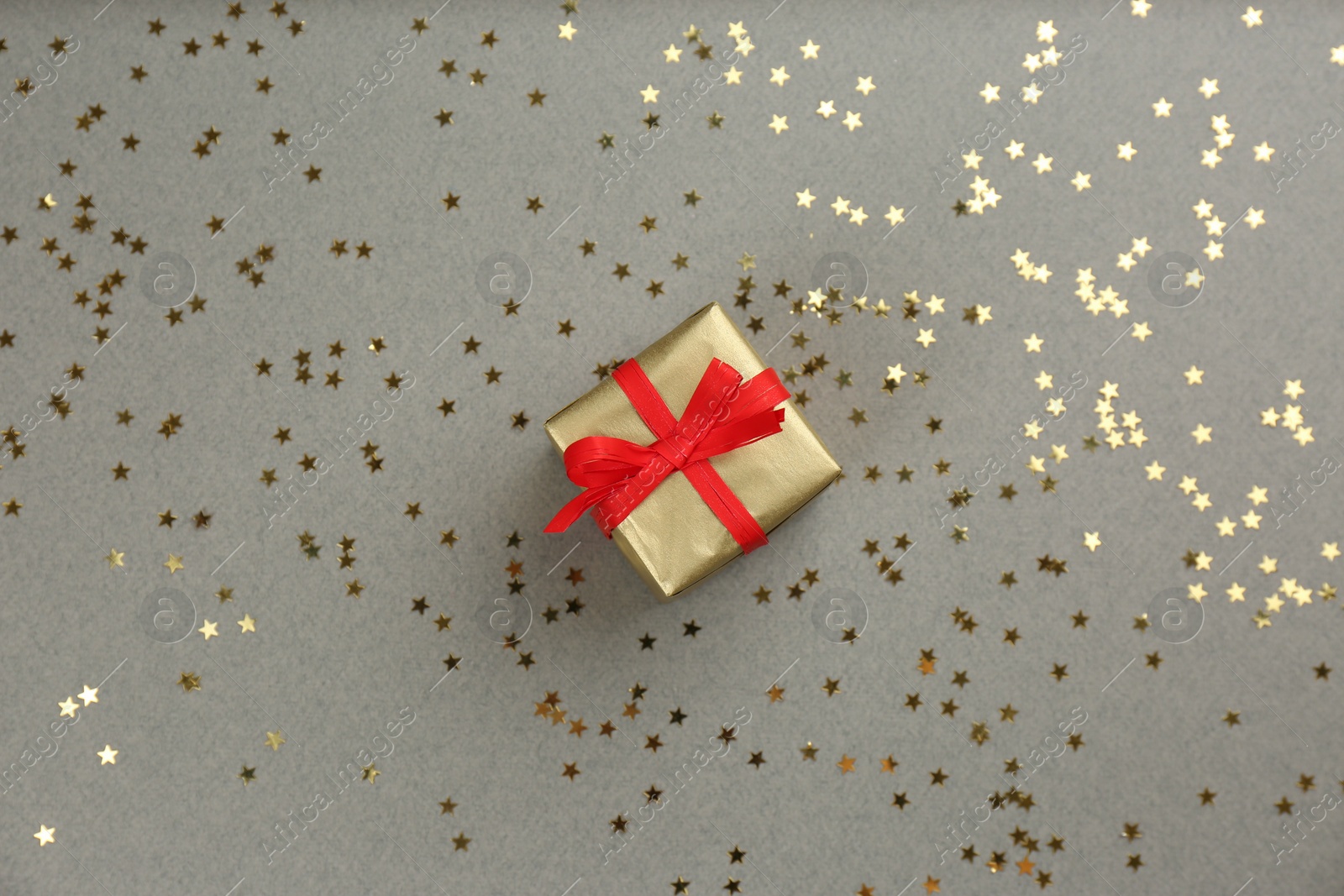 Photo of Golden gift box and shiny confetti on grey background, top view. Space for text