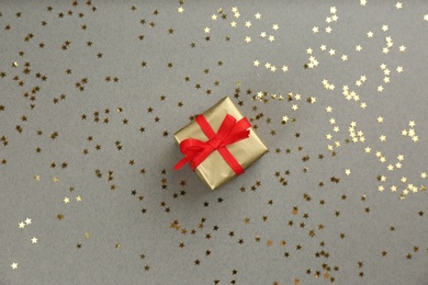 Photo of Golden gift box and shiny confetti on grey background, top view. Space for text