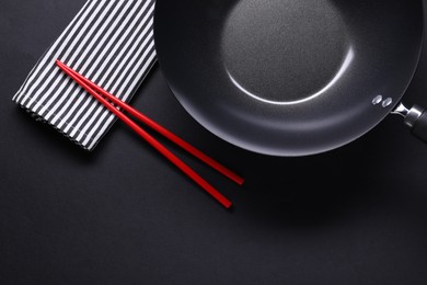 Empty iron wok and chopsticks on black table, flat lay