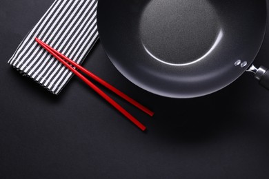 Photo of Empty iron wok and chopsticks on black table, flat lay