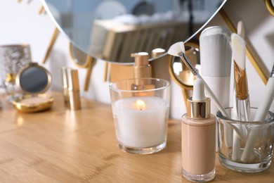 Photo of Burning soy candle, cosmetics and accessories on wooden dressing table