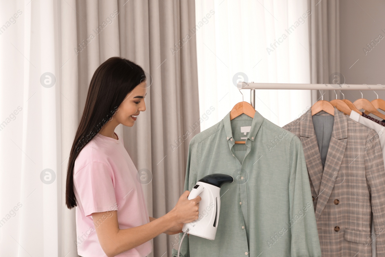 Photo of Woman steaming shirt on hanger at home