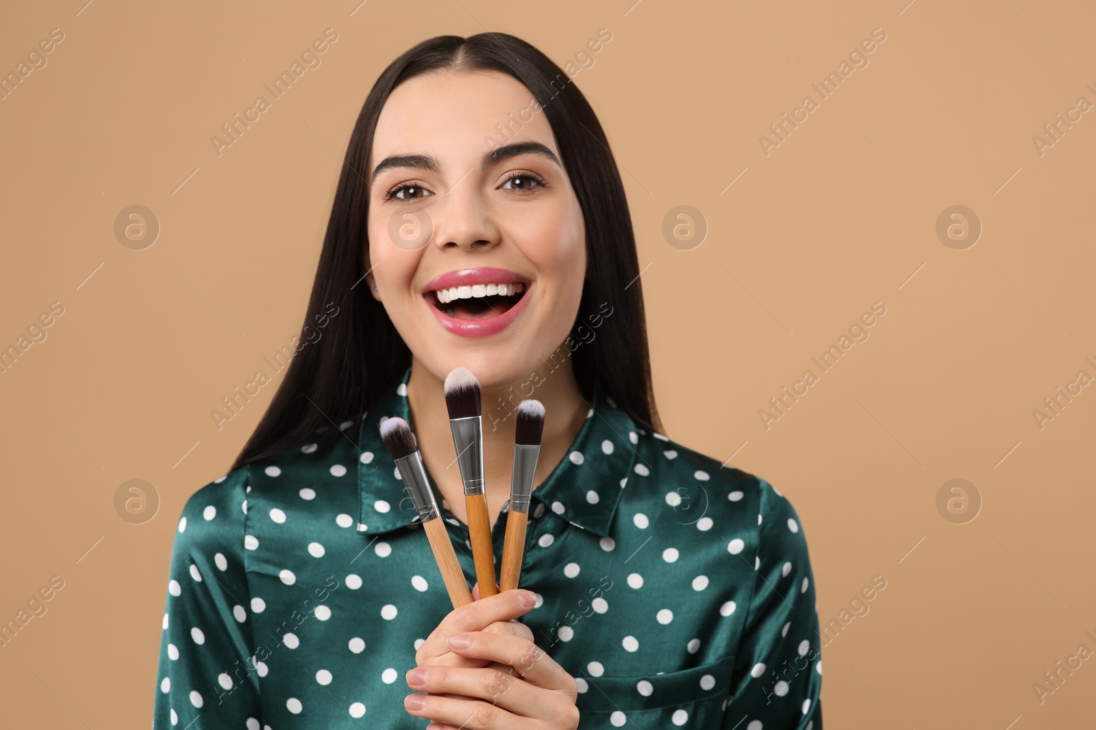 Photo of Happy woman with different makeup brushes on light brown background. Space for text