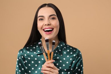 Happy woman with different makeup brushes on light brown background. Space for text