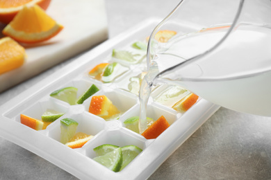 Pouring juice into ice cube tray with lime and orange on light table, closeup