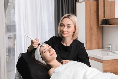 Photo of Cosmetologist applying mask on woman's face in clinic