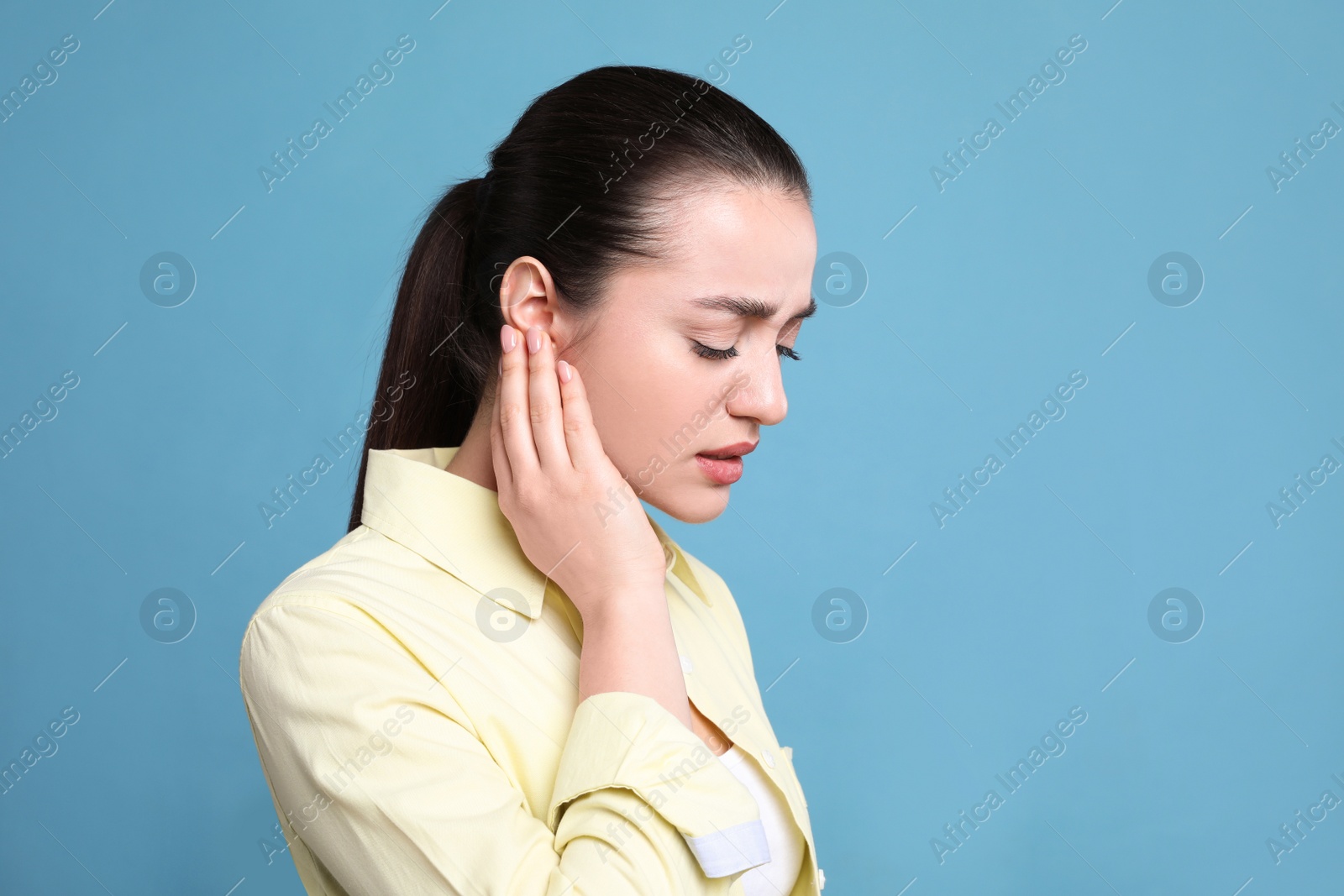 Photo of Young woman suffering from ear pain on light blue background. Space for text