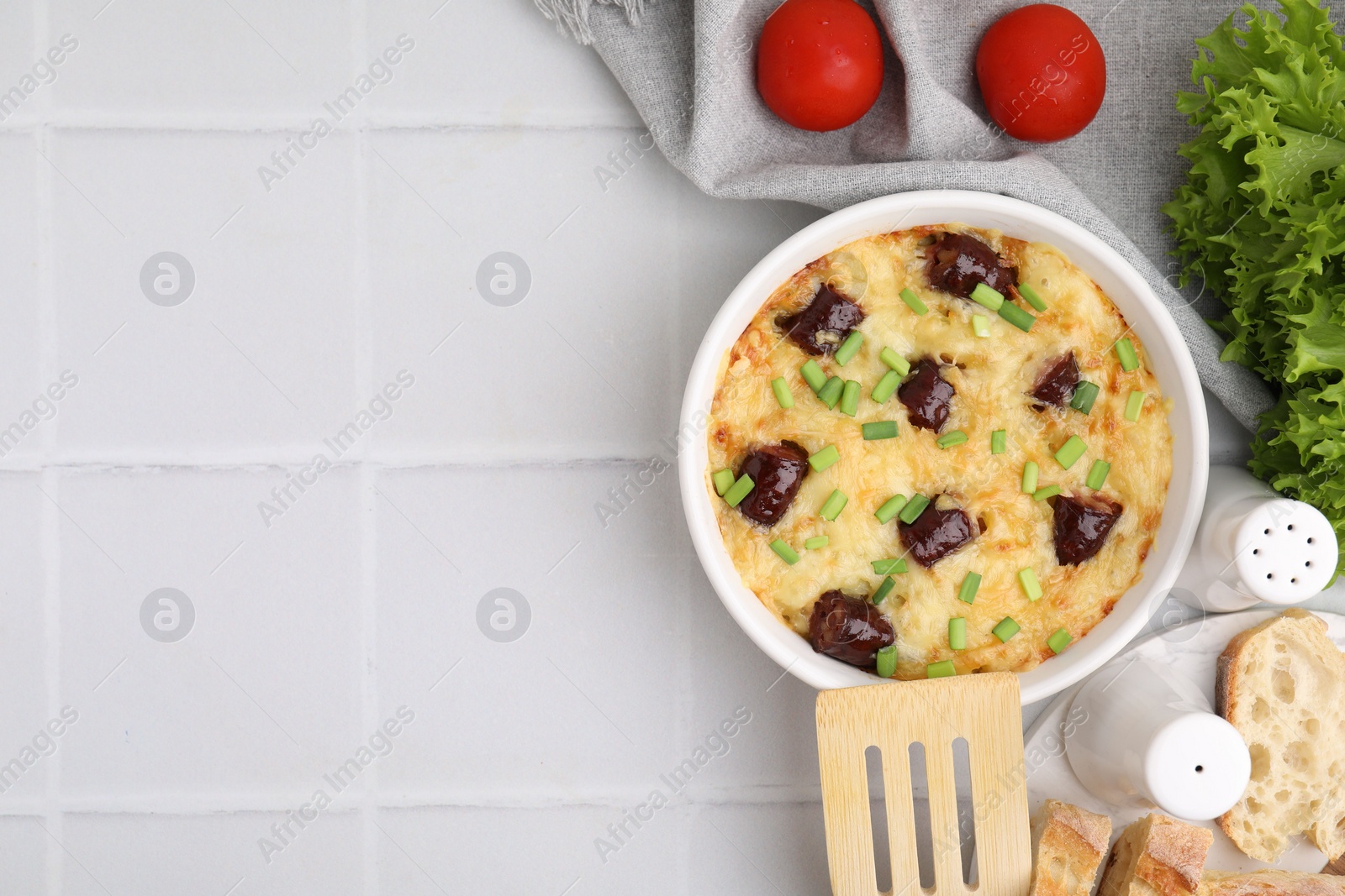 Photo of Tasty sausage casserole with green onions in baking dish served on white tiled table, flat lay. Space for text