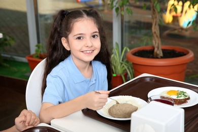 Photo of Cute girl at table with healthy food in school canteen