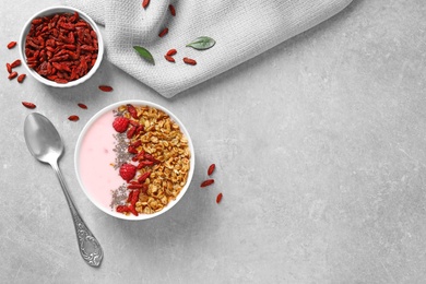 Smoothie bowl with goji berries and spoon on grey table, flat lay. Space for text