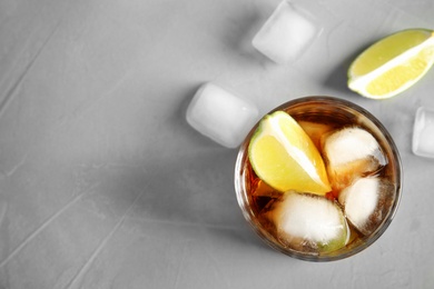 Glass of cocktail with cola, ice and cut lime on light background, flat lay. Space  for text