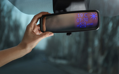 Image of Young woman adjusting smart rear view mirror in car, closeup