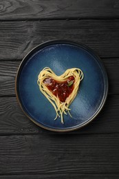 Photo of Heart made with spaghetti and sauce on black wooden table, top view