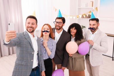 Photo of Coworkers taking selfie during office party indoors