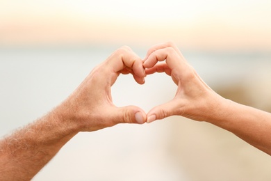 Photo of Happy couple making heart with their hands against blurred landscape