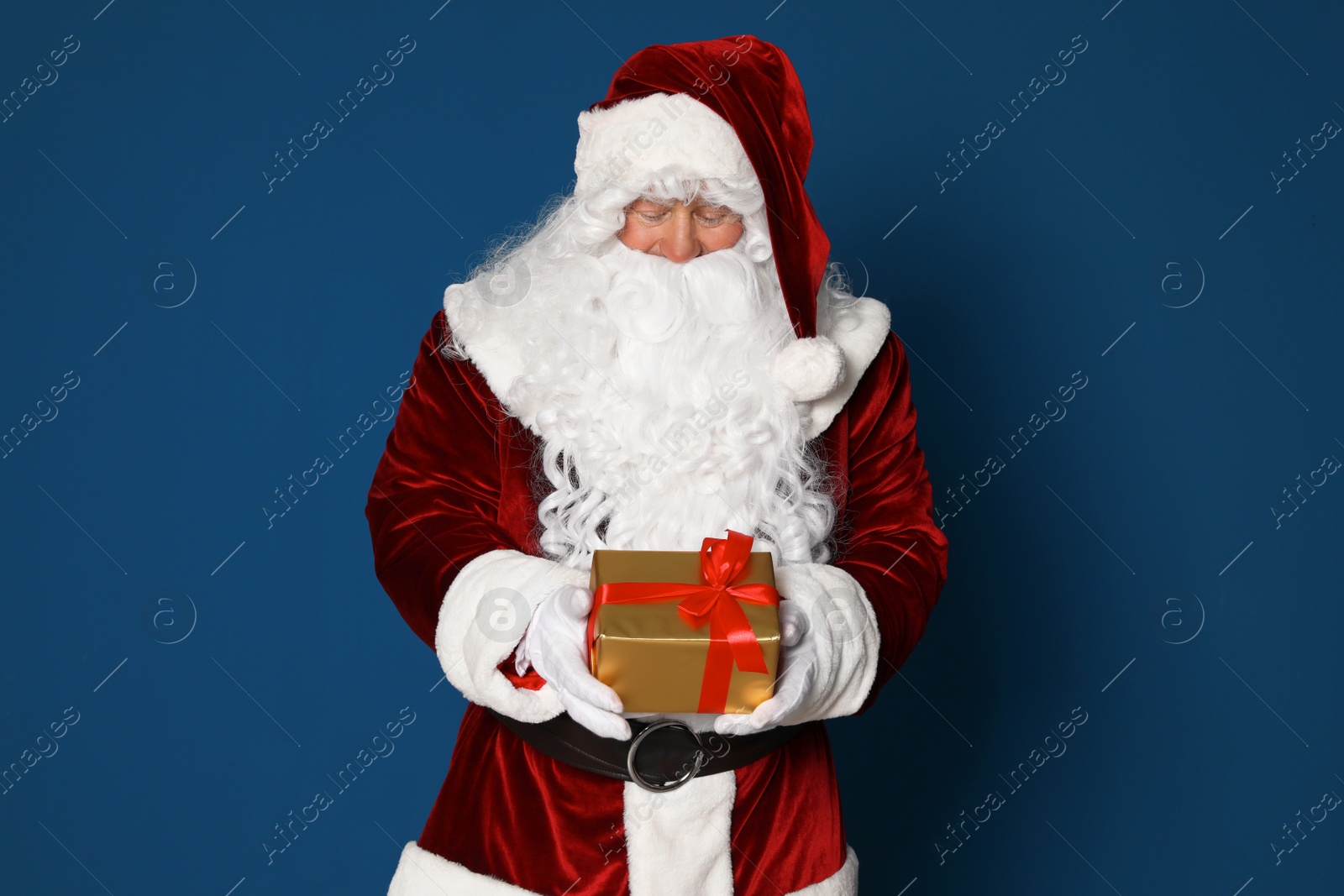 Photo of Authentic Santa Claus with gift box on blue background