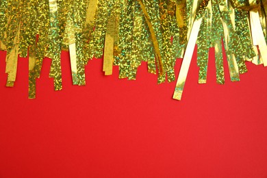 Photo of Golden tinsel on red background, top view. Space for text