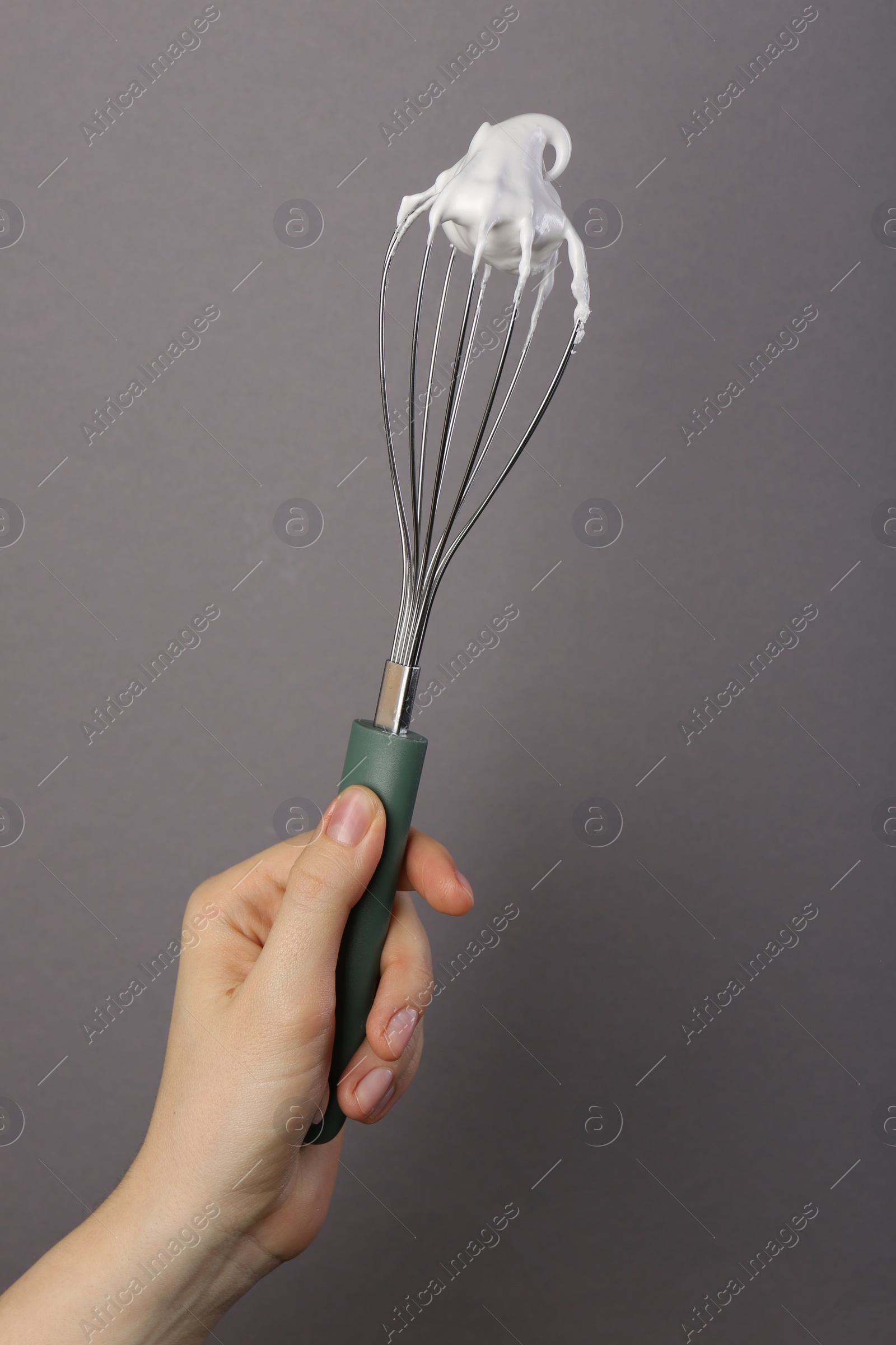 Photo of Woman holding whisk with whipped cream on grey background, closeup