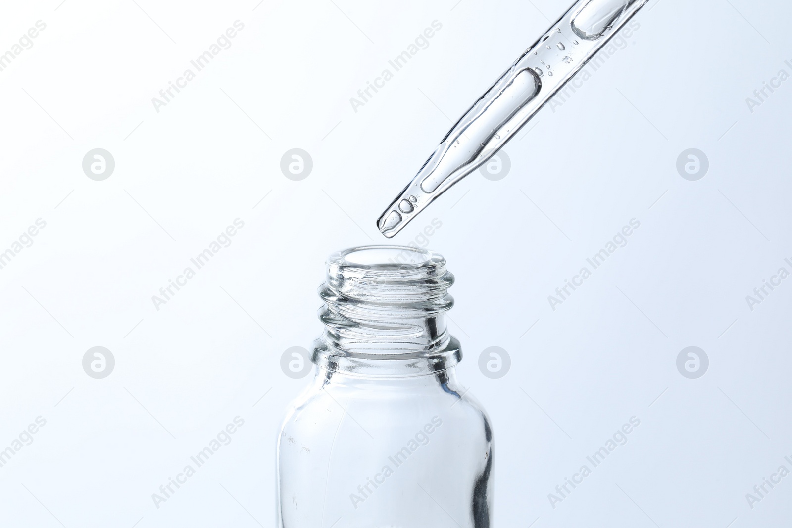 Photo of Dripping liquid from pipette into glass bottle on light blue background, closeup