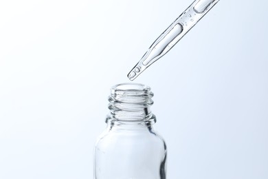 Dripping liquid from pipette into glass bottle on light blue background, closeup