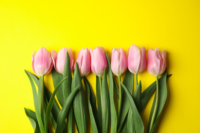 Photo of Beautiful pink spring tulips on yellow background, flat lay