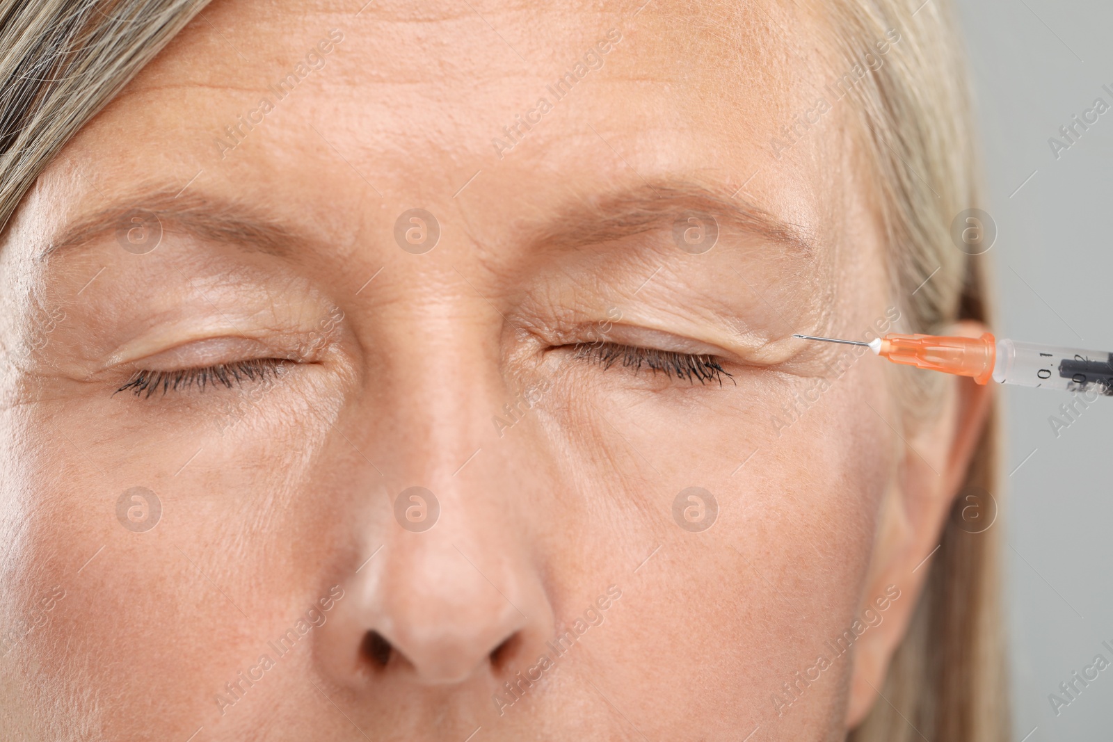 Photo of Senior woman getting facial injection on light grey background, closeup. Cosmetic surgery