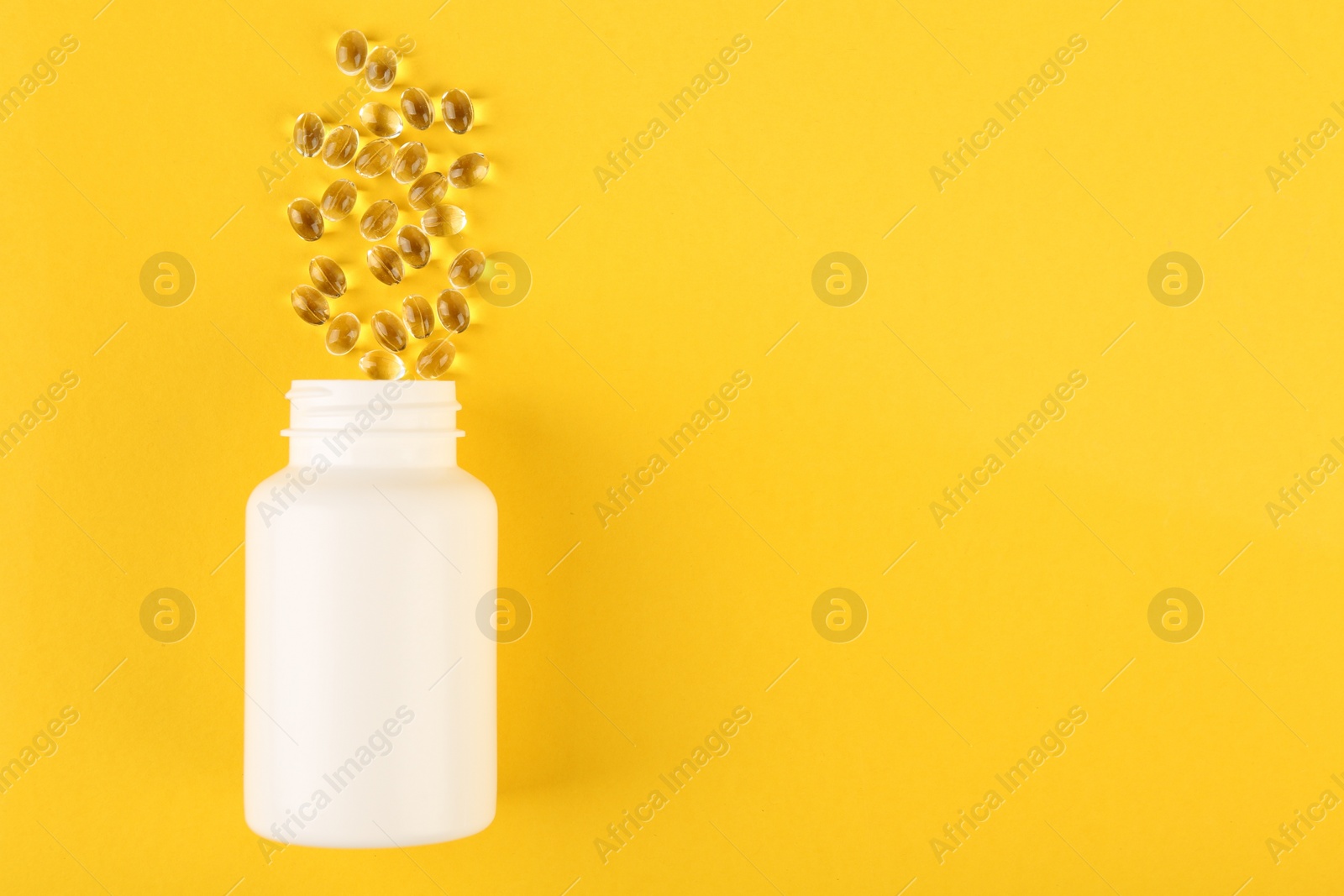 Photo of White medical bottle and vitamin capsules on yellow background, top view. Space for text