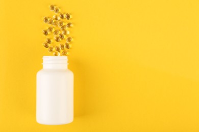 White medical bottle and vitamin capsules on yellow background, top view. Space for text