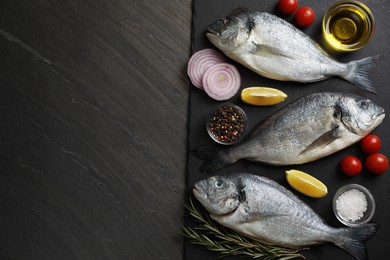 Photo of Fresh raw dorado fish, lemon, spices and tomatoes on black table, flat lay. Space for text